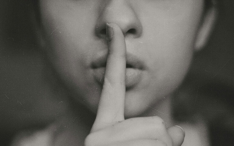 Woman's finger to lips symbolizing the silent thyroid epidemic and overlooked symptoms.